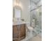 Bathroom with a marble-tiled walk-in shower, stone sink, wooden cabinets, and a modern arched mirror at 13430 S Garnet Rd, Buckeye, AZ 85326