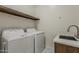 Bright laundry room with modern washer and dryer, utility sink, faucet, and a floating shelf for storage at 13430 S Garnet Rd, Buckeye, AZ 85326