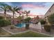 Beautiful backyard pool featuring lush greenery, palm trees, a lounge chair, and a stunning sunset at 2103 E Canyon Pl, Chandler, AZ 85249