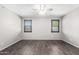 A neutral bedroom showcases two windows, dark wood-look floors, and a ceiling fan at 17345 W Spur Dr, Surprise, AZ 85387