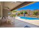 A covered patio features a dining table and chairs next to a pool, with landscaping providing privacy at 27562 N 99Th Dr, Peoria, AZ 85383