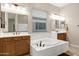 Bright bathroom featuring double vanities, a soaking tub, and neutral tile flooring at 41584 W Springtime Rd, Maricopa, AZ 85138
