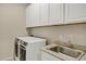 Functional laundry room features modern machines, a sink and ample white cabinet storage above at 41584 W Springtime Rd, Maricopa, AZ 85138