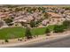 Aerial view of neighborhood park featuring grass, trees, walking path, covered picnic tables and playground at 6944 S Morning Dew Ln, Buckeye, AZ 85326