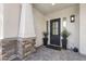 Charming covered porch with stone accents, a black front door, and decorative potted plants at 20795 W San Juan Ave, Buckeye, AZ 85396