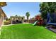 Large backyard featuring artificial turf, covered patio with outdoor kitchen, play structure and trampoline at 17937 W Westpark Blvd, Surprise, AZ 85388