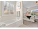 Bright bathroom with a soaking tub, plantation shutters, decorative wall art and a glimpse of a bedroom at 6948 E Quill St, Mesa, AZ 85207