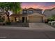 Charming two-story home boasts a desert landscape, mature tree, and tile roof under a vibrant sunset sky at 10329 E Star Of The Desert Dr, Scottsdale, AZ 85255