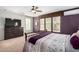 This main bedroom offers a window with a great view, dark purple accent wall, and stylish ceiling fan at 15456 W Corrine Dr, Surprise, AZ 85379