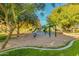 A colorful playground with slides and climbing structures sits atop a bed of sand and sits near mature shade trees at 15456 W Corrine Dr, Surprise, AZ 85379