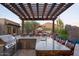 Stylish outdoor kitchen equipped with a grill, granite countertop, and pergola with ambient string lights, perfect for entertaining at 26285 N 89Th St, Scottsdale, AZ 85255