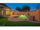 A dreamy backyard featuring a freeform pool with a rock waterfall, lush green turf, ambient string lights, and privacy at 6309 W Hughes Dr, Phoenix, AZ 85043