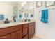 Bathroom featuring a granite top vanity with double sinks, cherry cabinets, and a decorative mirror at 17693 W Lincoln St, Goodyear, AZ 85338