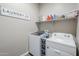 Functional laundry room with modern appliances, storage shelves, and decor sign at 40848 W Hillman Dr, Maricopa, AZ 85138
