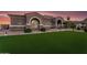 Well-lit home with desert landscaping and manicured lawn enhancing the curb appeal against a beautiful sunset sky at 19903 E Augustus Ave, Queen Creek, AZ 85142