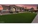 Stunning home featuring lush green lawn, desert landscaping, and stone accents under a picturesque sunset sky at 19903 E Augustus Ave, Queen Creek, AZ 85142