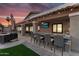 Outdoor bar area with seating, TV, and built-in grill, perfect for entertaining with a colorful sunset backdrop at 19903 E Augustus Ave, Queen Creek, AZ 85142