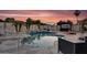 Backyard featuring a refreshing pool, multiple lounge chairs, lush palms, and a barbecue area with a beautiful sunset at 19903 E Augustus Ave, Queen Creek, AZ 85142