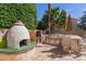 An outdoor kitchen features a pizza oven, grill, sink, and dining area surrounded by lush greenery at 987 E Divot Dr, Tempe, AZ 85283