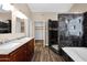 Bathroom featuring dual sinks, wood cabinets, a walk in closet, and a black tile shower at 1755 N 74 Th Pl, Mesa, AZ 85207