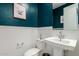 Stylish half-bathroom with blue walls, white trim, pedestal sink, toilet, mirror, and decorative artwork at 22682 E Indiana Ave, Queen Creek, AZ 85142
