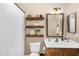 Neutral bathroom featuring a single sink vanity, decorative floating shelves, toilet and shower with white curtain at 3859 N El Sereno St, Mesa, AZ 85207