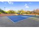 A tennis court surrounded by desert trees and shrubs with a covered bench for relaxing between sets at 3859 N El Sereno St, Mesa, AZ 85207