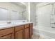 Well-lit bathroom with double sinks, oak cabinets, and a tiled bathtub with shower at 15941 N 171St Ln, Surprise, AZ 85388