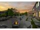 Outdoor oasis with a built-in BBQ, fire pit, and covered patio overlooking the pool and lush landscaping at dusk at 2282 E Zion Way, Chandler, AZ 85249