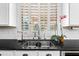 Well-lit kitchen sink under window with plantation shutters, black counters, and stainless faucet at 2282 E Zion Way, Chandler, AZ 85249