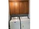 A compact laundry room with top loading washer/dryer set and overhead storage cabinets at 1156 E Vinedo Ln, Tempe, AZ 85284
