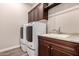 Well-lit laundry room features modern washer and dryer, storage cabinets, and a sink with a granite countertop at 13448 W Miner Trl, Peoria, AZ 85383