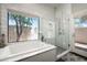 Bright bathroom featuring a bathtub, glass-enclosed shower, and views of the trees at 8601 E De La O Rd, Scottsdale, AZ 85255