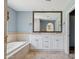 Bright bathroom featuring double vanity, large framed mirror, soaking tub with tan tile and travertine floors at 10450 E Terra Dr, Scottsdale, AZ 85258
