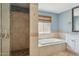 Bright bathroom featuring walk in shower with tan travertine surround, soaking tub, and window at 10450 E Terra Dr, Scottsdale, AZ 85258
