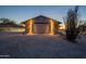 Well-lit home garage at dusk with a graveled driveway and desert landscape at 15612 S Tuthill Rd, Buckeye, AZ 85326
