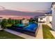 Backyard pool featuring a modern fire pit, striped umbrellas, and lush landscaping at dusk at 3684 E Boot Track Trl, Gilbert, AZ 85296