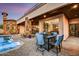 An elegant outdoor patio with a dining table, stone pillars, and a beautiful pool under a colorful evening sky at 6551 E Flat Iron Loop, Gold Canyon, AZ 85118