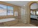 Relaxing main bathroom featuring a soaking tub, glass block shower, and a view into the main bedroom at 16401 S 29Th Ave, Phoenix, AZ 85045