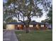 Dusk view of brick home with covered carport, mature tree, and soft interior lighting at 1839 E Palo Verde Dr, Phoenix, AZ 85016