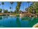The Sun Village community sign is surrounded by mature palm trees and a serene body of water at 14561 W Winding Trl, Surprise, AZ 85374