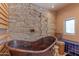 Close-up of a copper bathtub with stone accent wall, sconces, and natural light from a window at 7302 E Rose Ln, Scottsdale, AZ 85250