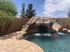 Backyard pool with water feature, mature trees, and lush desert landscaping at 35743 W Cartegna Ln, Maricopa, AZ 85138
