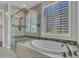 A luxurious bathroom featuring a sleek soaking tub, neutral tile accents, and a glass shower at 16881 W Merrell St, Goodyear, AZ 85395