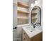 Stylish bathroom featuring a modern vanity with open wooden shelving and an elegant arched mirror at 5520 E Muriel Dr, Scottsdale, AZ 85254