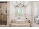 Elegant soaking tub surrounded by travertine, with chandelier and a window at 2107 E Park Ave, Gilbert, AZ 85234