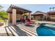 A covered patio is poolside with pergola, ceiling fan, stone flooring, and comfortable lounge chairs at 2107 E Park Ave, Gilbert, AZ 85234
