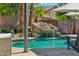 Backyard pool with a rock waterfall feature, palm trees, and lounge seating at 14364 W Cameron Dr, Surprise, AZ 85379