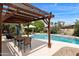 Backyard swimming pool with patio featuring a wooden pergola and lush landscaping for outdoor enjoyment at 1656 W Meseto Cir, Mesa, AZ 85202
