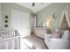 Bedroom with white crib, dresser, soft green walls, and a plush chair by a bright window at 20510 W White Rock Rd, Buckeye, AZ 85396
